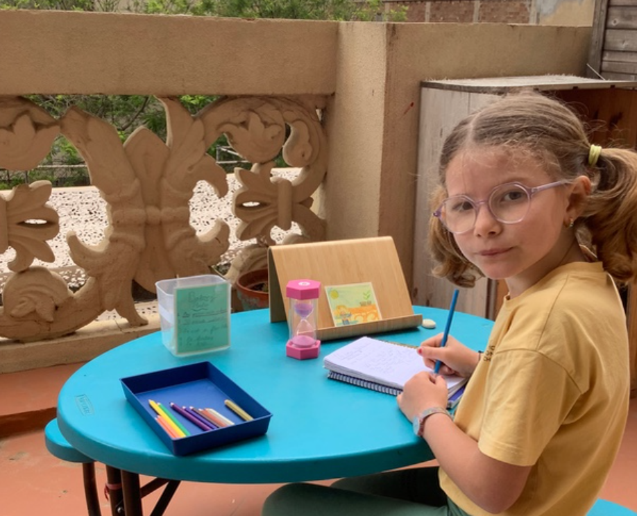 A child working independently at an outdoor table with a timer, notebook and pencils