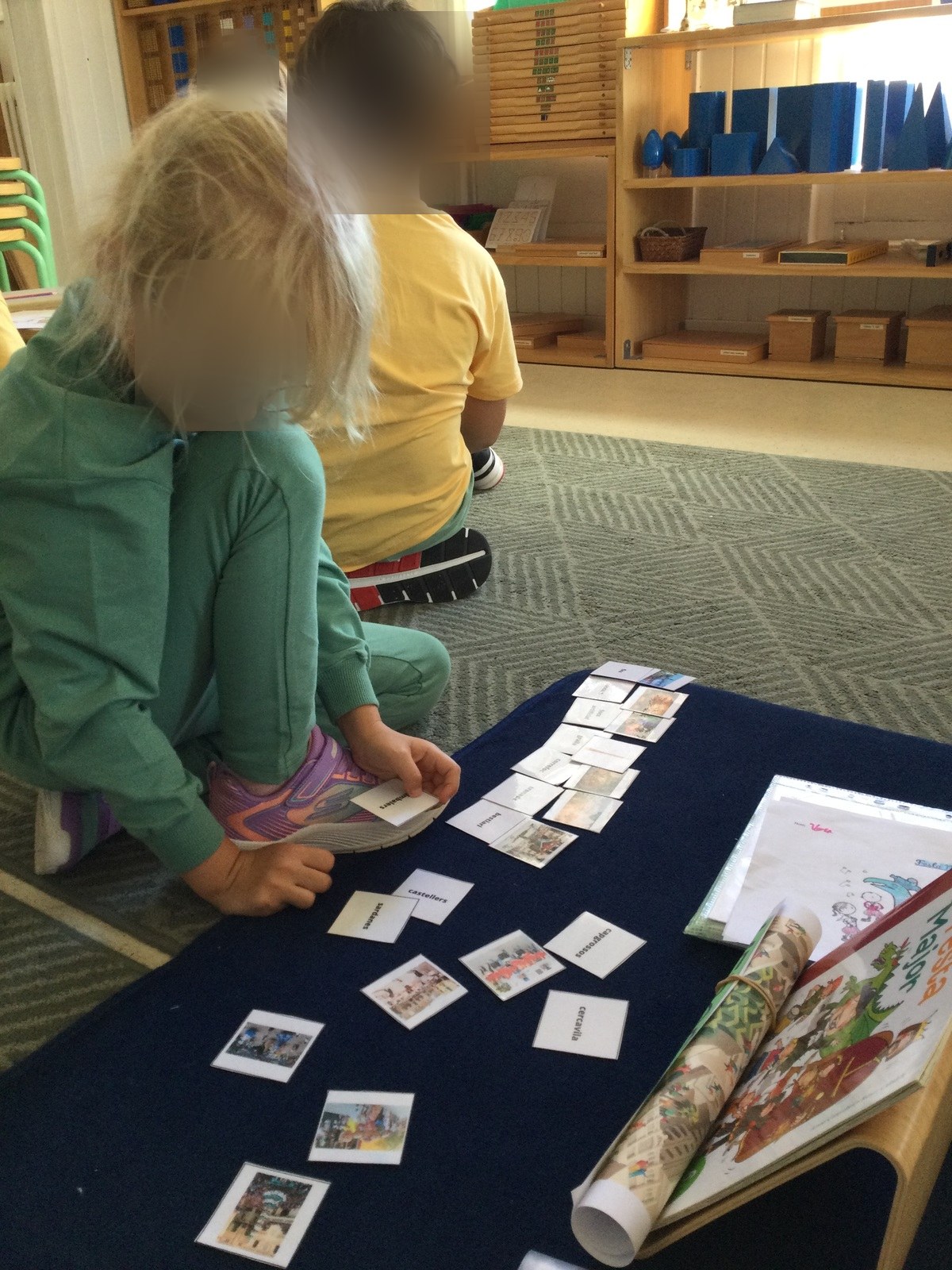 Niños y niñas de Casa de Niños con las tarjetas de vocabulario de la Fiesta Mayor sobre una alfombra