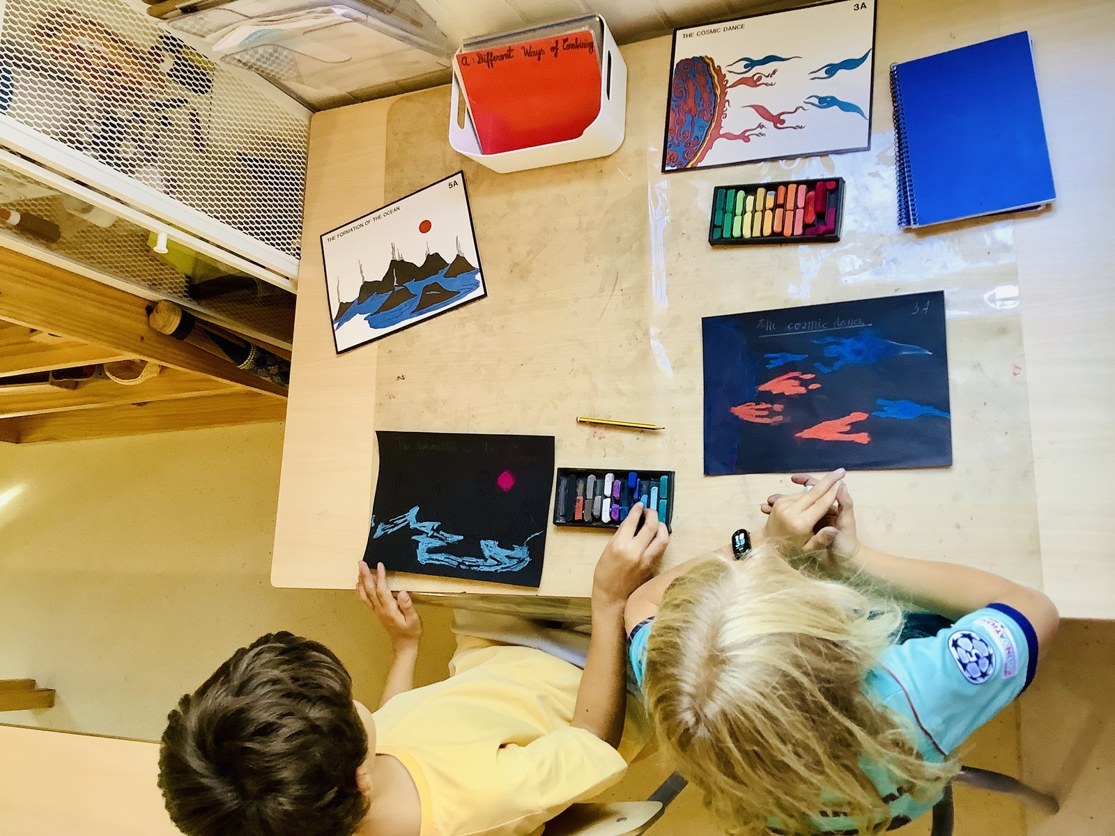 Trabajos al pastel de los niños sobre la Danza Cósmica y la Formación del Océano, junto a las láminas impresionistas Montessori
