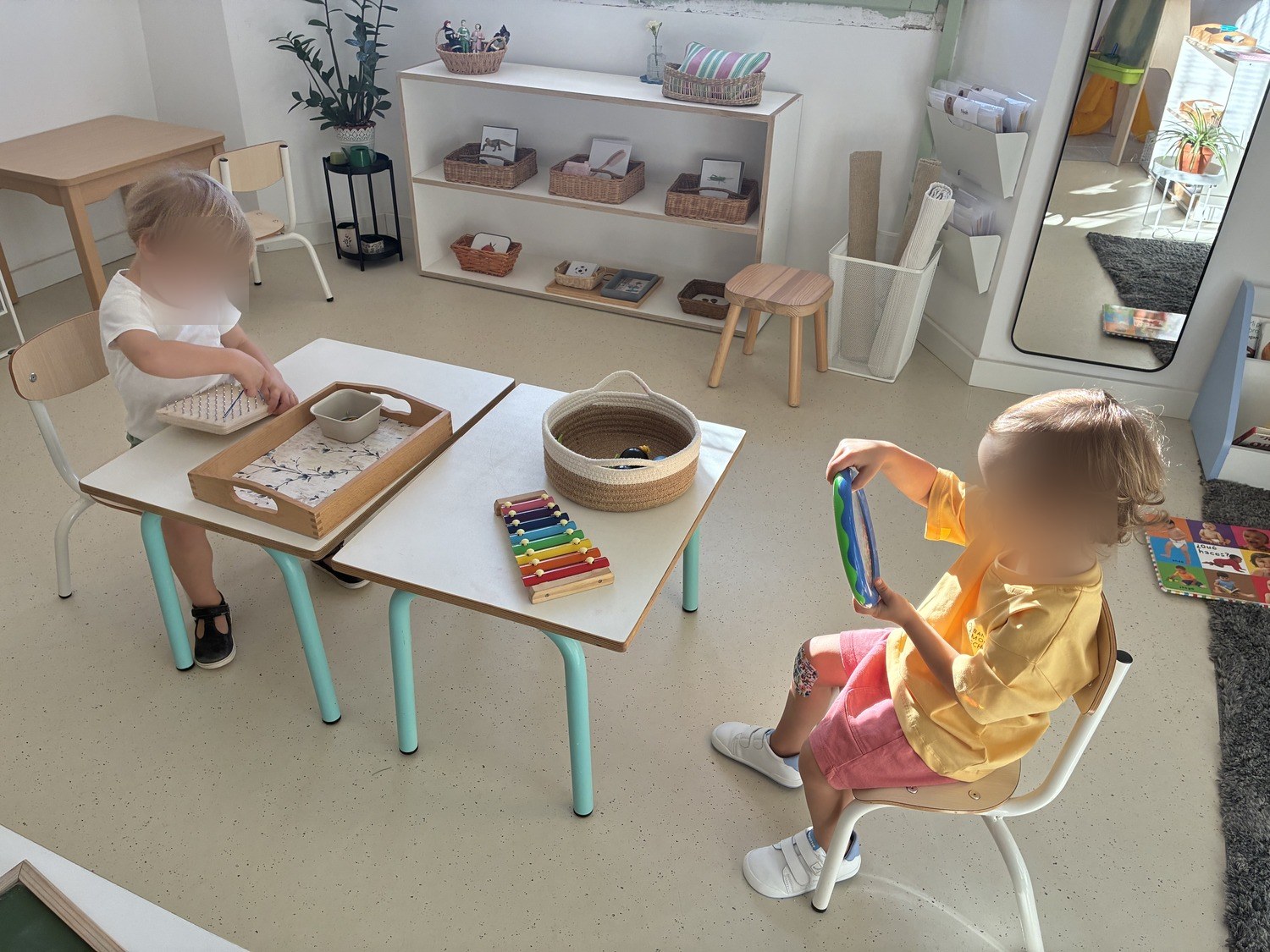 Un niño explorando un xilófono mientras otro trabaja en la mesa de al lado