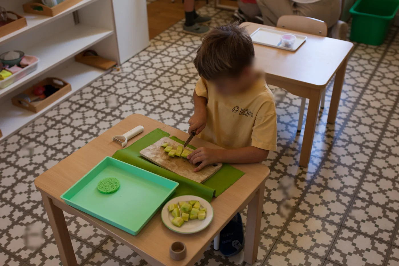 A child cutting fruit at a small table in the Children’s House at Barcelona Montessori School