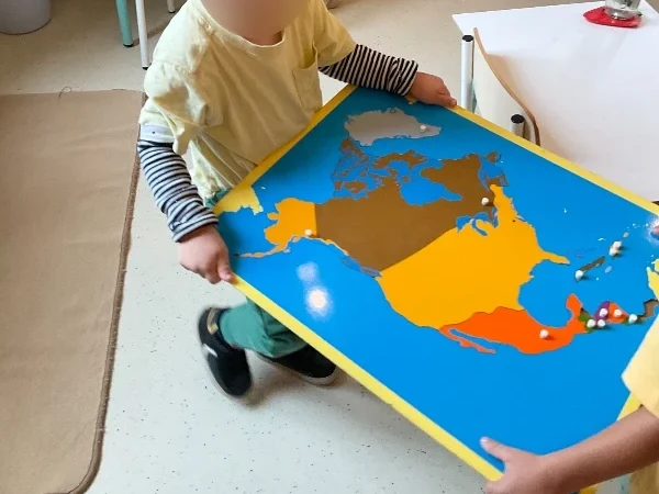 Un alumno de Casa de Niños llevando el mapa-puzle de América del Norte en Barcelona Montessori School